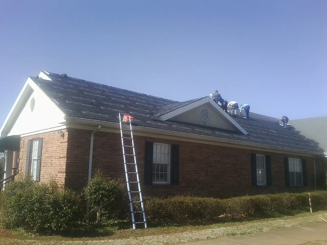 Crew tearing shingles off a brick ranch roof with a ladder set — Emergency Roof Repair work by our crew in West Monroe