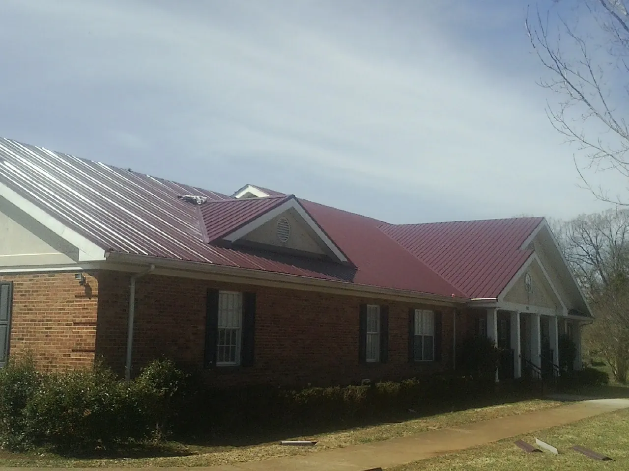 Red metal roof with gabled entries on a long brick building, from a Hail Damage Roof Repair job in West Monroe
