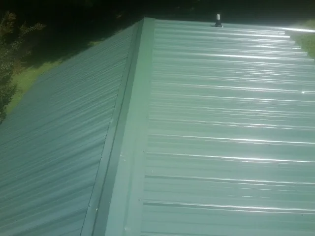 New green metal panels meeting at the ridge of a roof — Flat Roof Repair work by our crew in West Monroe