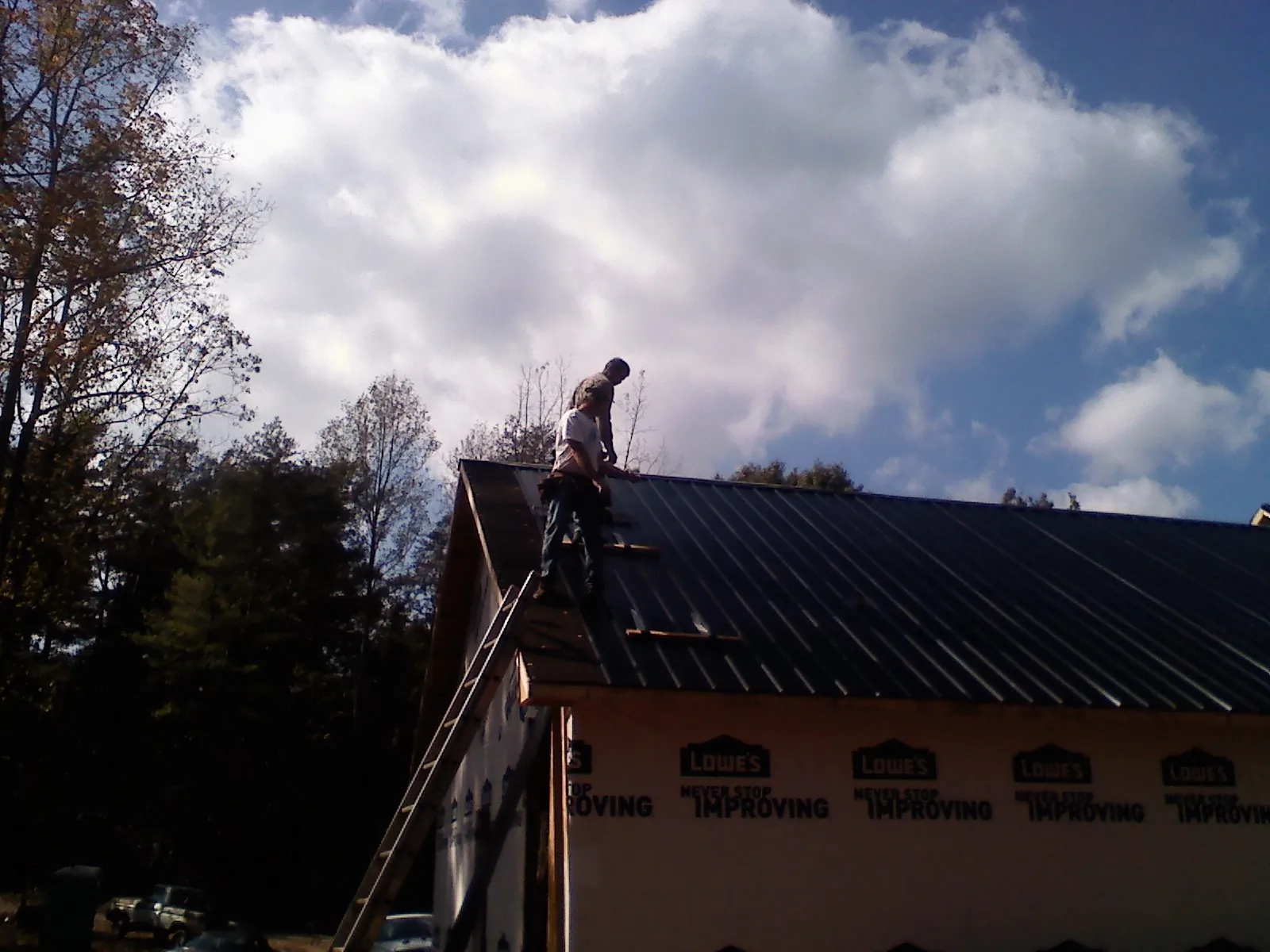 Roofer fastening dark metal panels high against a cloudy sky, from a Roof Inspection job in West Monroe