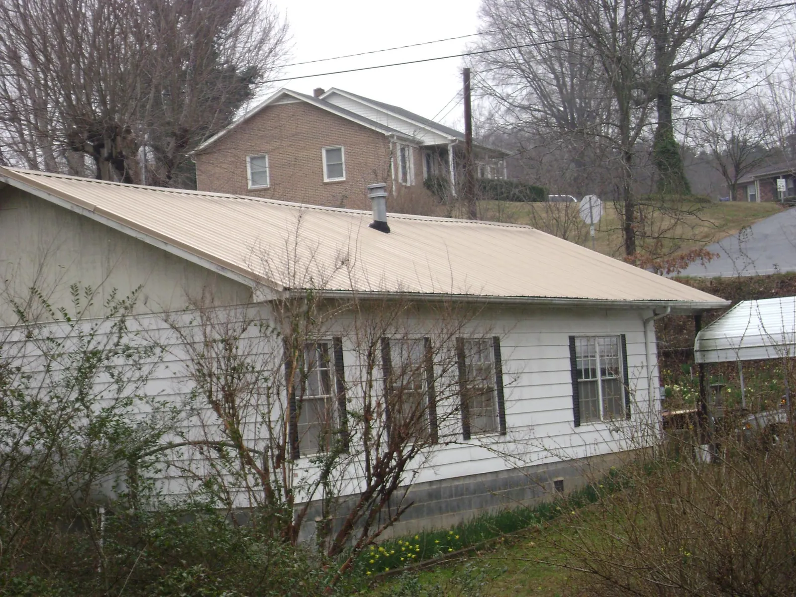 Tan metal roof on a white sided house set into a hillside — Commercial Roofing by Roofing Brothers in West Monroe